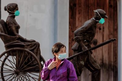 Una mujer con mascarilla camina junto a estatuas enmascaradas en Shanghái, China.