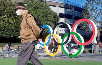 Un hombre con tapaboca da la espalda a unos anillos olímpicos instalados en Tokio. Foto: EFE.