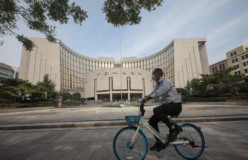 Un hombre pedalea su bicicleta frente a la sede del Banco Popular de China, en Pekín, China.