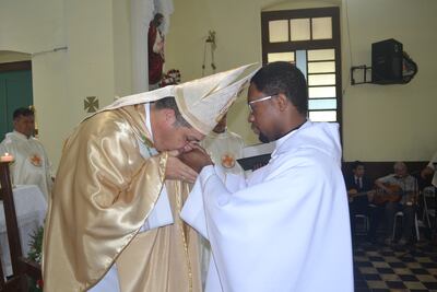 El obispo Gabriel Escobar besa las manos del nuevo sacerdote haitiano Mac-Donald durante la celebración de ordenación en la catedral de Fuerte Olimpo.