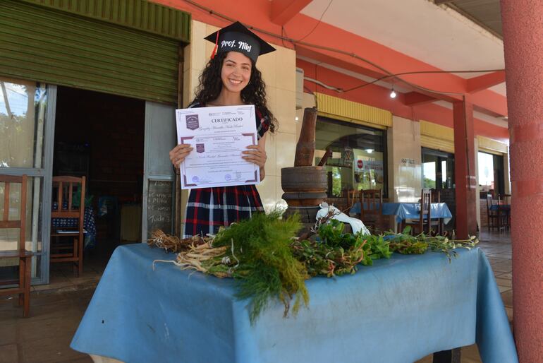 Nicole Rashel González Amarilla exhibe con alegría su título de docente en su puesto de venta de remedios yuyos.