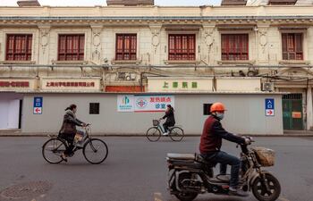 Dos mujeres en bicicleta y un hombre en moto pasan junto a un contenedor convertirdo en una clínica de emergencia para tratar a personas con Covid en Shanghai (China).