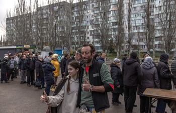 Tom Hughes, voluntario escocés posa con una joven ucraniana mientras forman fila para recibir pizzas en Kherson, al sur de Ucrania.