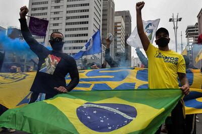 People raise their clenched fists as they demonstrate with a Brazilian flag against Brazilian President Jair Bolsonaro and racism, in Sao Paulo, Brazil, on June 14, 2020, amid the novel coronavirus pandemic. (Photo by NELSON ALMEIDA / AFP)