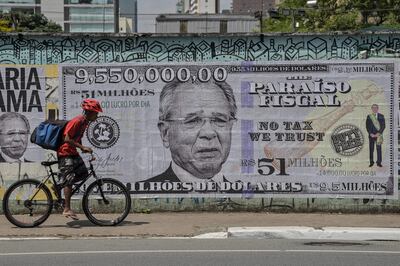 A man rides his bike past a poster depicting Brazil's Economy Minister Paulo Guedes on a US$9.55 million bill, in Sao Paulo, Brazil, on October 8, 2021, just days after he was mentioned in the "Pandora Papers" media investigation exposing world leaders' use of tax havens. - According to the investigation, Guedes has deposited US$9.55 million in his offshore Dreadnoughts International Group, opened in 2014 in the British Virgin Islands, which was equivalent to R$23 million at the time. With the devaluation of the real, accelerated during his tenure at the Ministry of Economy, the value today corresponds to R$51 million. (Photo by NELSON ALMEIDA / AFP)