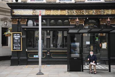 Una mujer espera el autobús en una parada situada delante de un pub en Londres.