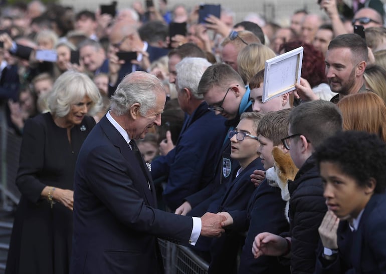 El rey Carlos III (c) y la reina consorte, Camilla (i), saludan a varias personas