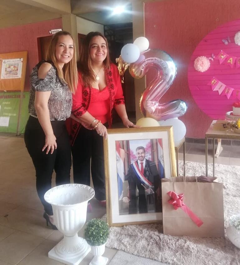Sonia Medina (derecha) y Elena Villalba posan con un retrato del presidente Mario Abdo Benítez en el festejo de los dos años de gestión de la segunda al frente de la Coordinación de Educación de Cordillera. 