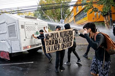 Artistas callejeros con un letrero que decía: No más policías militares. Disolución de la policía en la nueva constitución. Choque con un cañón de agua de la policía durante una protesta contra la violencia policial tras el asesinato de un artista callejero por parte de la policía local, en Panquipulli en Santiago, el 6 de febrero de 2021.