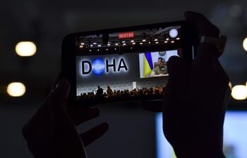 Una persona graba al presidente de Ucrania, Volodymyr Zelensky, dirigiéndose a distancia a la sesión inaugural del Foro de Doha.