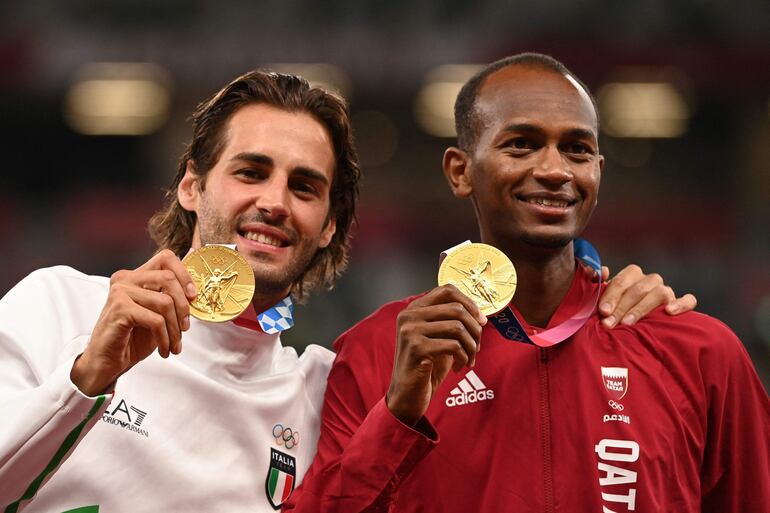 Los medallistas de oro de salto con garrocha, Gianmarco Tamberi y Mutaz Essa Barshim posan en el podio durante la premiación de la categoría de salto alto en Tokio 2020, en el estadio olímpico.