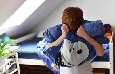 Un niño con su peluche y su almohada favorita, frente a la cama de su habitación.
