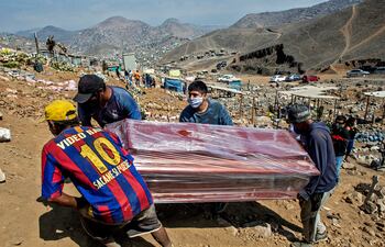 Los parientes de un fallecido con sospecha de coronavirus cargan su ataúd envuelto en plástico en el cementerio de Nueva Esperanza en las afueras de Lima, Perú.