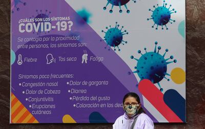 Una mujer espera frente a un cartel con información sobre COVID-19 a tres meses de la cuarentena decretada por la pandemia de COVID-19, en La Paz (Bolivia).