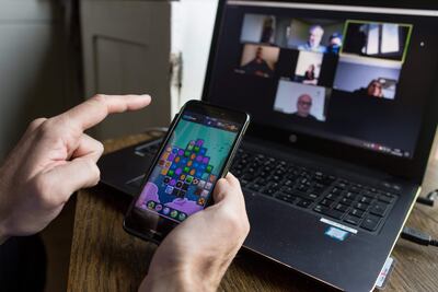 Un hombre juega en su celular mientras participa de una videollamada en su casa.