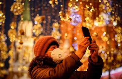Una mujer con mascarilla toma fotografías en una calle adornada con motivo de la Navidad en Moscú, Rusia.
