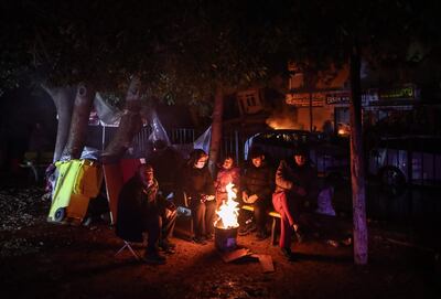 Personas se calientan alrededor de una fogata mientras el personal de emergencia busca víctimas en el sitio de un edificio derrumbado después de un terremoto en el distrito de Iskenderun de Hatay, Turquía, el 6 de febrero de 2023.