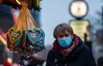 Una mujer con mascarilla camina junto a un puesto de venta de artículos navideños en Berlín, Alemania.