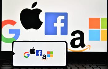 Logos de Google, Apple, Facebook, Amazon y Microsoft en la pantalla de un celular y una laptop.