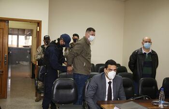 Un agente policial procede a quitar las esposas a uno de los acusados por apriete a narcos. Archivo Abc.