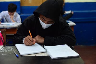 Un alumno con tapabocas completa su cuaderno en el salón de clases.