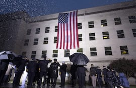 Supervivientes y miembros del Ejército escuchan el himno nacional junto a una bandera desplegada en el Pentágono, en Arlington, Virginia, Estados Unidos este domingo durante el 21º aniversario del atentado a las Torres Gemelas y el Pentágono del 11-S.