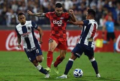 El paraguayo Héctor Villalba (c), jugador de Libertad, pelea por el balón con dos futbolistas de Alianza Lima durante el partido de la fase de grupos de la Copa Libertadores en el estadio Alejandro Villanueva, en Lima, Perú.