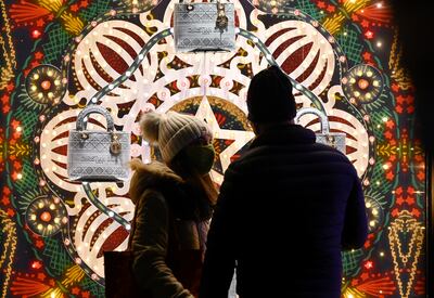 Una pareja con tapabocas pasea frente a las vidrieras de la Piazza di Spagna en Roma, decorada con motivos navideños.