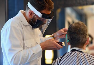 Un peluquero con máscara de protección corta el pelo de un cliente en una barbería en Nueva York.