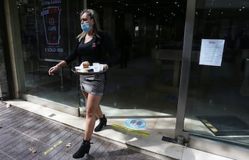 Una empleada de los llamados "café con piernas" (cafetería atendida por mujeres de ropa ceñida) trabaja hoy lunes, durante la apertura de los negocios que no son de primera necesidad en el centro de Santiago de Chile. Tras más de seis meses cerrados por la pandemia, reabrieron este lunes en el centro de Santiago de Chile los polémicos "cafés con piernas", las turísticas cafeterías surgidas en la dictadura militar que perduran pese a las quejas del potente movimiento feminista.