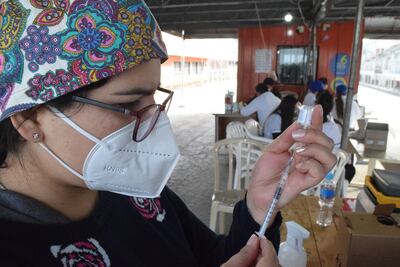 Una vacunadora prepara una jeringa en el vacunatorio del centro cívico. Al fondo, el equipo de apoyo técnico.