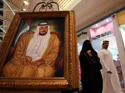 Un hombre y una mujer caminan junto a un retrato del presidente emiratí Khalifa bin Zayed al Nahyan, fallecido hoy.