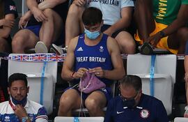 El saltador británico tejiendo un suéter, sentado en una tribuna.