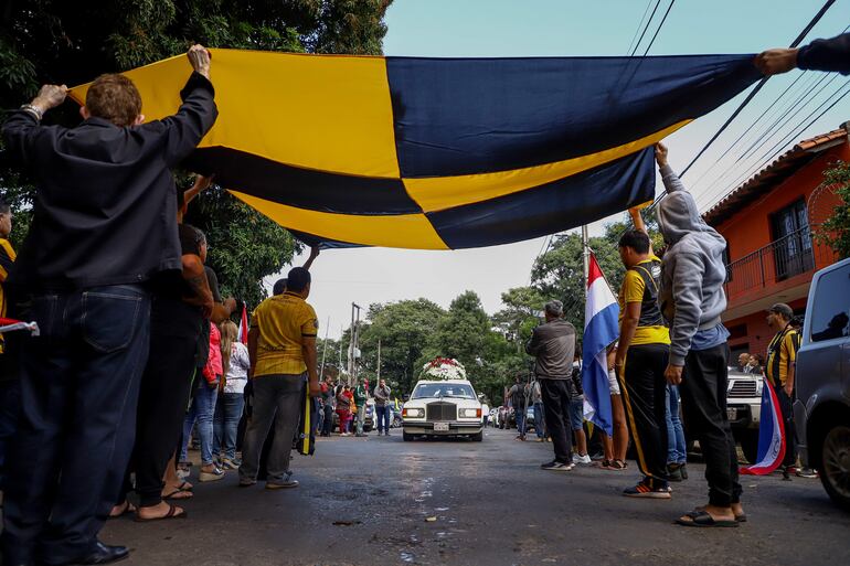 Aficionados del Guaraní acompañan hoy el carro fúnebre que transporta los restos del asesinado fiscal Marcelo Pecci, frente a la sede del club en Asunción (Paraguay). 