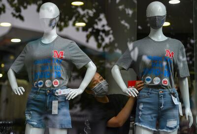 Un miembro del personal con una mascarilla arregla una camiseta con un eslogan que dice: "Uniendo las manos para prevenir COVID-19 (nuevo coronavirus)" en un maniquí en una tienda minorista en Hanoi, Vietnam.