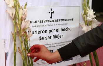 Una persona coloca una flor cerca de un cartel en honor a las víctimas de feminicidios.