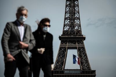 Un hombre y una mujer con máscaras faciales caminan en la Plaza del Trocadero mientras una bandera nacional francesa ondea en la Torre Eiffel.