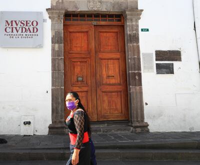 Una mujer con mascarilla pasa frente al Museo de la Ciudad cerrado por las restricciones impuestas por el gobierno ecuatoriano frente al COVID-19