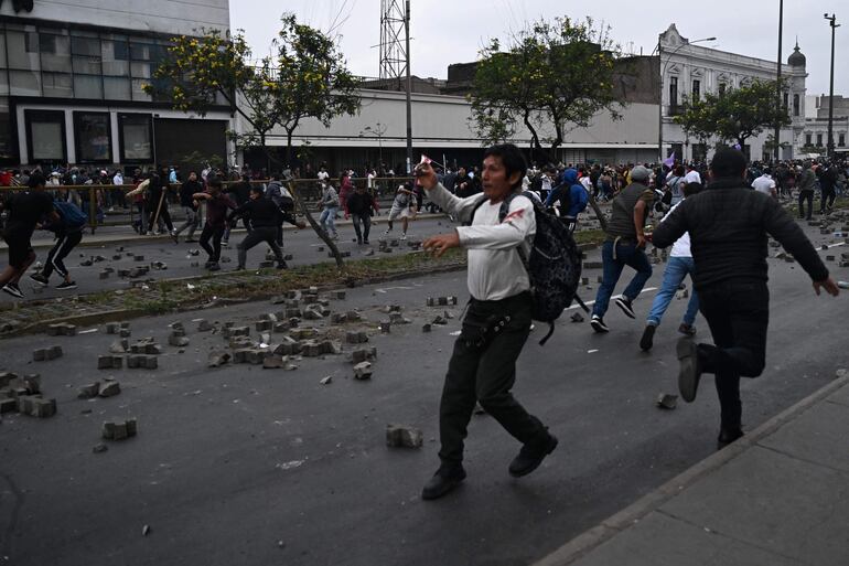 Supporters of Peruvian President Pedro Castillo clash with the police in the outskirts of the Lima Prefecture, where Castillo is under detention, in Lima, on December 7, 2022. - Peru's President Pedro Castillo dissolved Congress on December 7, 2022, announced a curfew and said he will form an emergency government that will rule by decree, just hours before the legislature was due to debate a motion of impeachment against him. (Photo by ERNESTO BENAVIDES / AFP)