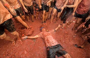 Un participante de la Tomatina se acuesta en el piso entre tomates explotados, mientras otros participantes lo rodean, en las calles del pueblo español de Buñol.