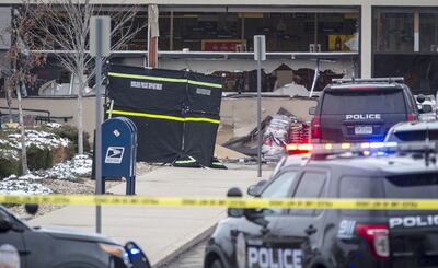 Vehículos policiales ante el supermercado con las ventanas hechas añicos por los disparos.