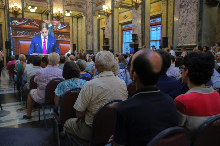 Simpatizantes del presidente de Uruguay, Luis Lacalle Pou, siguen el balance del mandatario que hace ante la Asamblea General, tras cumplirse un nuevo aniversario de su asunción como jefe de Estado, en una pantalla instalada en el Palacio Legislativo, hoy en Montevideo (Uruguay). Dentro del recinto Lacalle Pou fue esperado por la vicepresidenta de Uruguay y presidenta de la Asamblea General, Beatriz Argimón, y por un grupo de legisladores de diferentes partidos. (EFE)