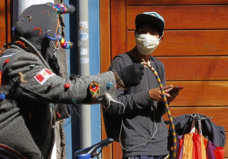 Una persona disfrazada de "Kusillo", un personaje tradicional andino, recuerda a los transeúntes que usen mascarillas y guantes en Puno, Perú.