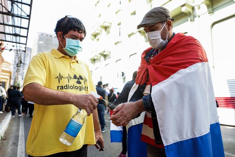 Dos hombres se desinfectan las manos mientras participan en una manifestación de trabajadores del sector salud, frente al Ministerio de Hacienda en Asunción (Paraguay)