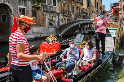 Gondoleros van con los clientes a un paseo en góndola por un canal en Venecia.