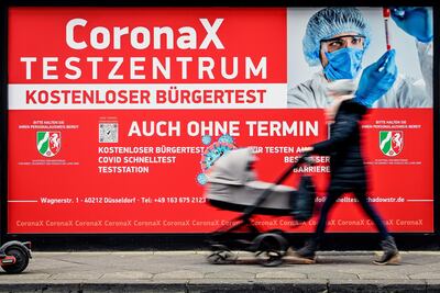 Una mujer empuja un carrito de bebé frente al cartel que anuncia una estación de testo móvil de Covid-19 en Duesseldorf, Alemania.