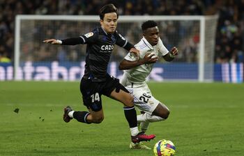 El centrocampista japonés de la Real Sociedad, Takefusa Kubo (i), disputa el balón ante el delantero brasileño del Real Madrid, Vinicius Jr., durante el encuentro correspondiente a la jornada 19 de primera división que disputaron ayer en el estadio Santiago Bernabéu, en Madrid. EFE / Juanjo Martín.