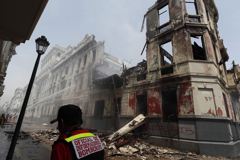 Bomberos trabajan en los alrededores de una casona que se incendió durante la jornada de protestas, hoy, en Lima (Perú).