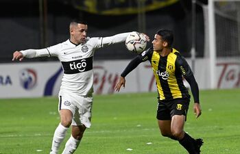 Derlis González extiende los brazos en su intento por controlar el balón, ante la cobertura defensiva de Marcelo Benítez. El “10” franjeado no tuvo una noche inspirada, aunque le puso ganas.