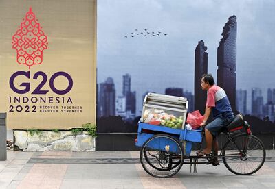 Un vendedor de frutas en bicicleta pedalea con su mercadería frente a un cartel con el logo del G20, en Yakarta, Indonesia.